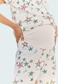 Těhotenský outfit z bílého materiálu s barevnými hvězdnými vzory v růžové, zelené a modré barvě. Elastický design se přizpůsobí rostoucímu bříšku.