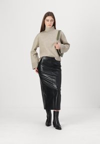 Beige strikket genser med høy hals og klokke-ermer, kombinert med et svart midi skjørt i faux lær med krokodillemønster og knehøye svarte støvler.