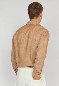 Camicia di lino marrone chiaro con finitura texture, maniche lunghe e colletto classico, dotata di polsini con bottoni e un taglio informale.