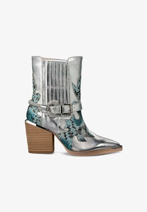 Zilveren leren enkelboot met hoge, geribbelde schacht, textuur in blauw en zwart, en een chunky bruine hak. Heeft een decoratieve gesp.