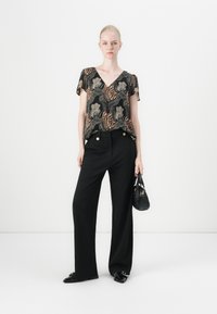 Top a maniche corte con scollo a V, con un motivo nero, beige e marrone; pantaloni neri a vita alta con bottoni dorati; borsa nera.
