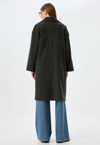 Donkergrijze wollen jas met een klassieke kraag, een losse silhoutte en verlaagde schouders, gecombineerd met lichtblauwe wijde jeans.