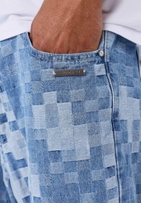 Pantaloni in denim con motivo a quadretti in tonalità di azzurro chiaro e blu scuro. Dotati di una targhetta argentata con la scritta "PROJECT X PARIS".