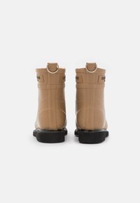 Botas de tobillo de goma en color marrón claro con un acabado texturizado, punta redonda, tirador en la parte trasera y suelas negras, que cuentan con un detalle de costura a lo largo de los lados.