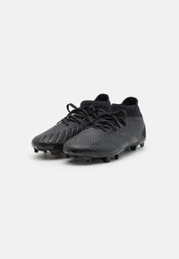 Schwarze Fußballschuhe mit einer strukturierten Oberfläche, ausgestattet mit einem gestrickten Kragen und traditionellen Schnürsenkeln, die für Grip mit geformten Stollen an der Außensohle konzipiert sind.