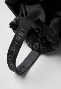 Zwarte stoffen tas met een getailleerde bovenkant, verstelbare schouderband en plastic knoopaccenten; textuurriem met reliëfmerkdetails.
