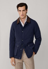 Marineblauer gesteppter Mantel mit einem braunen Cordkragen, Frontreißverschluss, Druckknopfverschlüssen und zwei Fronttaschen.