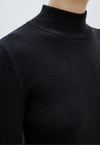 Pull à col roulé noir côtelé avec une coupe ajustée et une texture douce, doté d'un col haut et d'épaules sans coutures.