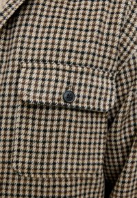 Bruin en beige geruite flanellen shirt met een borstzak, voorzien van een zwarte knop, zachte textuur en een klassiek design.