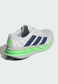 White running shoe with navy blue Adidas stripes and neon green accents on sole and heel, labeled "ADISTAR" and "REPETITOR."