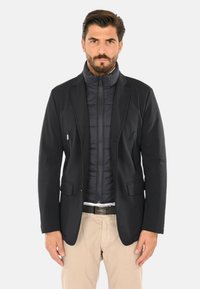 Giacca nera multi-strato con design blazer e interno trapuntato. Due tasche anteriori con zip, silhouette elegante.