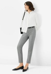 Graue maßgeschneiderte Hose mit schmaler Passform, kombiniert mit einer weißen Bluse mit Knopfleiste und schwarzen spitzen Flats. Schwarzer Gürtel und Umhängetasche sind im Preis enthalten.