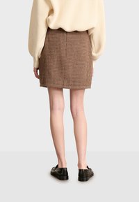 Falda mini de textura marrón con silueta ajustada, combinada con un suéter de punto oversize en color crema y mocasines negros.