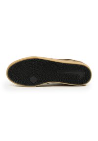 Black sneaker sole with a zigzag tread pattern, featuring a light brown rubber border and a logo detail near the heel.