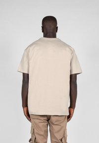 Beige bomulds t-shirt med en rund halsudskæring og korte ærmer, synlige syningsdetaljer, båret med lyse khaki cargo bukser.