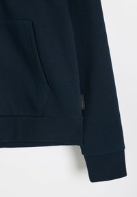 Granatowa bluza z kapturem wykonana z miękkiego materiału, z kieszenią kangurką, prążkowanymi mankietami i dołem, z małą metką marki po boku.