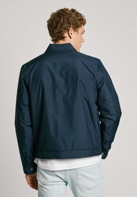 Chaqueta azul marino con una textura suave y brillante, cuello y puños abotonados. Este diseño cuenta con un corte recto y una longitud por debajo de la cintura.
