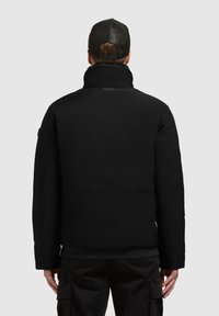 Zwarte pufferjack met een hoge kraag en een gladde textuur. Ontworpen met een ontspannen pasvorm en minimale hardwaredetails. Achteraanzicht weergegeven.