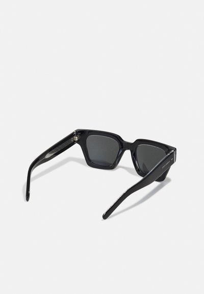 Black rectangular sunglasses with dark lenses, glossy plastic frame, textured side accents, and slender arms featuring branding details.