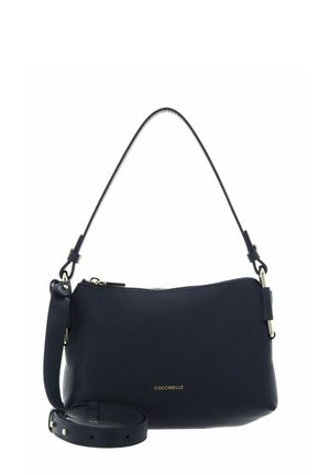 Sac à main Coccinelle en cuir noir avec fermeture éclair sur le dessus, bandoulière réglable et poignée courte sur fond blanc.