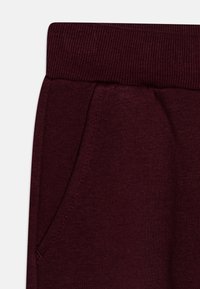 Vinröd tyg med ribbad elastisk midjeband och diagonala sömmar för sidofickor.