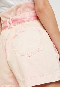 Pantalones cortos de mezclilla color rosa claro con una cinturilla de malla texturizada, acabado desteñido y un único bolsillo trasero con diseño triangular.