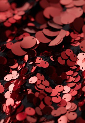 Czerwone, okrągłe cekiny o błyszczącej powierzchni rozsypane na czarnym, teksturowanym tle, ukazujące różne rozmiary i nakładające się detale.