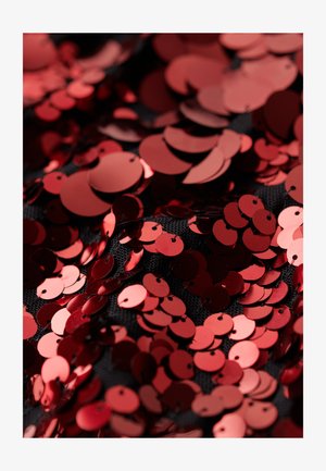 Røde cirkulære palietter med en glat finish spredt over en sort tekstureret stofbaggrund, der viser forskellige størrelser og overlapping detaljer.