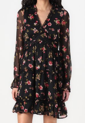 Robe noire à manches longues avec imprimé floral rose et rouge, manches transparentes, décolleté en V à volants, et jupe à volants en étages avec ourlet volanté.