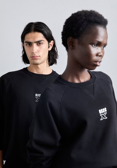 Black pullover sweatshirts with a textured finish, featuring a graphic logo on the chest, displayed on two models in a neutral backdrop.