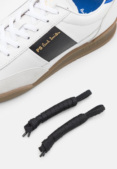 Weiße Lederturnschuhe mit schwarzem Akzent und goldenem Logo, ausgestattet mit einer Gummisohle. Enthält zwei schwarze Schnürsenkel mit Schlaufe.