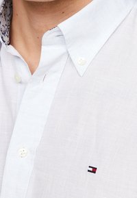 Vaaleansininen paita, jossa on teksturoitu kangas, napillinen kaulus ja valkoiset napit. Rinnassa pieni kirjailtu logo.