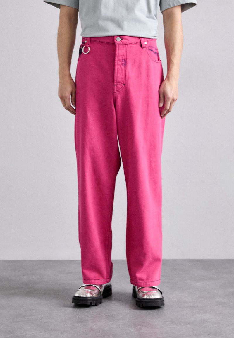 Φωτεινά ροζ τζιν παντελόνια με ίσια γραμμή, διαθέτουν πλευρικό D-ring και δύο μπροστινές τσέπες. Φορεμένα με μεταλλικά παπούτσια.