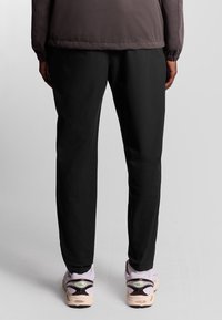 Zwarte, loszittende broek van lichtgewicht materiaal, met een gladde textuur en een elastische tailleband, gecombineerd met lichtgekleurde sneakers.