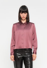 Camisa de manga longa, abotoada, em cetim de mauve profundo. Design com colarinho e um corte ligeiramente relaxado, com um brilho subtil, combinada com calças pretas brilhantes.