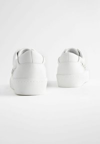 Weiße Sneaker bestehen aus einem glatten Lederoberteil, haben eine abgerundete Rückseite und eine dicke Gummisohle, mit gestickten Details und einem minimalistischen Design.