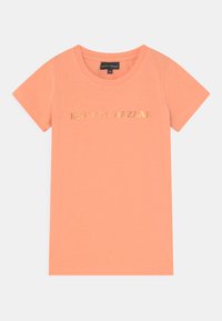 T-shirt de manga curta na cor pêssego, com um logótipo em folha de ouro "BRUINS BAZAAR" na frente. Feita de um tecido suave e leve.