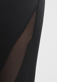 Mustaa kangasta, jossa on kolmionmuotoinen verkko-osio ja näkyvät ompeleet vaatteessa, joka on luultavasti urheiluvaatteita tai legginssejä.