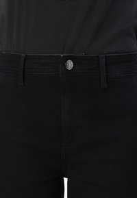 Black denim jeans featuring a button closure, five pockets, and a slim fit. Stitched detailing along the waistband and seams.