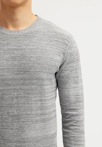 Pull gris à col rond en tissu tricoté doux avec un motif chiné subtil et des manches longues, présentant un col et des poignets côtelés.