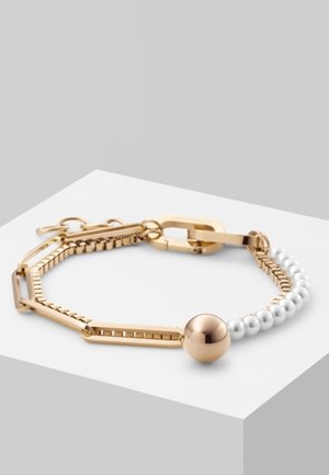 Bracelet en chaîne dorée avec des maillons rectangulaires, des perles blanches et une grosse perle sphérique dorée sur une surface blanche.