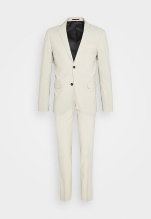 Beige suit with a notched lapel, single-breasted jacket, and two black buttons. Includes matching trousers, smooth fabric, and a black lining.