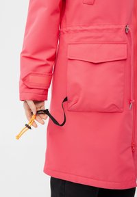 Capa impermeable rosa con cremallera frontal, cordón ajustable y un gran bolsillo lateral. Adjunto una cuerda elástica con un clip.