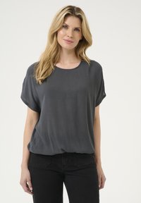 Grå kortärmad topp med en lös passform och textilstruktur, med en rund halsringning. Kombinerad med svarta denimjeans.