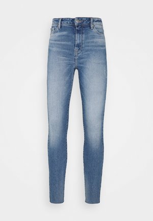 Blå højttaljede skinny jeans med falmede detaljer foran og knap- og lynlåslukning på hvid baggrund.