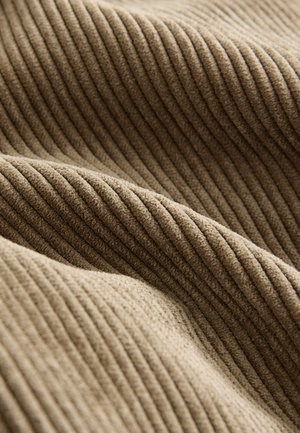 Bež rebrasta tkanina z mehko teksturo, ki prikazuje teksturirane črte in puhast občutek. Material ima topel, vabljiv videz.