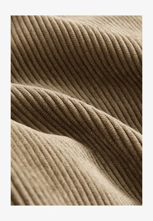 Bež rebrasta tkanina z mehko teksturo, ki prikazuje teksturirane črte in puhast občutek. Material ima topel, vabljiv videz.