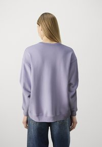 Sudadera lila de manga larga, con cuello redondo y dobladillo acanalado. Llevada sobre jeans azules. Tela suave con una textura lisa.