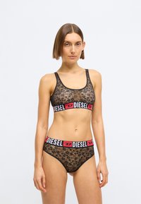 Μαύρο δαντελένιο bralette με φαρδιά ελαστική ζώνη που φέρει το κόκκινο λογότυπο "DIESEL". Αντίστοιχες μαύρες δαντελένιες ψηλόμεσες βρακάκια, και τα δύο με floral σχέδιο.