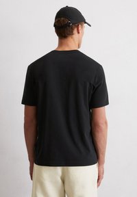 Zwarte katoenen t-shirt met korte mouwen en een ronde halslijn, gedragen met lichtgekleurde broeken, met een subtiel label aan de zijkant.